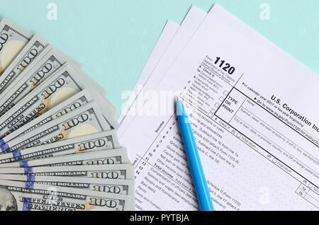 1120 tax form lies near hundred dollar bills and blue pen on a light blue background. US Corporation income tax return. Stock Photo