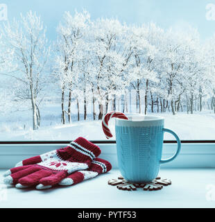 Winter background. Cup with candy cane on windowsill and winter trees outdoors. Winter festive composition Stock Photo