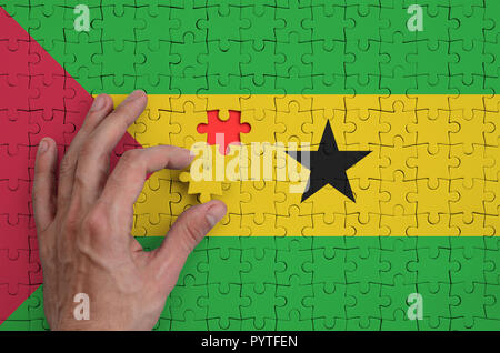 Sao Tome and Principe flag  is depicted on a puzzle, which the man's hand completes to fold. Stock Photo