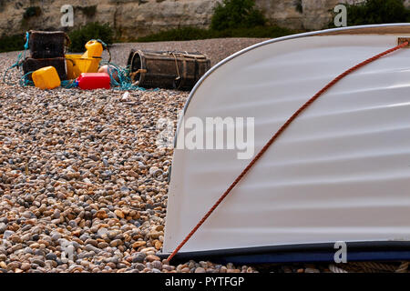 Upside down how of small boat on a stoney beach in England with some fishing gear and a crab/lobster pot in the background. Taken on Beer Beach, Devon Stock Photo