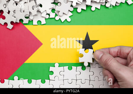Sao Tome and Principe flag  is depicted on a table on which the human hand folds a puzzle of white color. Stock Photo