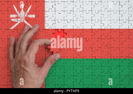 Oman flag  is depicted on a puzzle, which the man's hand completes to fold. Stock Photo