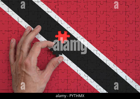 Trinidad and Tobago flag  is depicted on a puzzle, which the man's hand completes to fold. Stock Photo