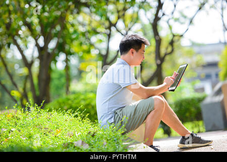 Young asian man using tablet in park Stock Photo