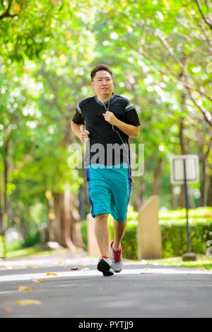 Asian man wearing headphones running in park Stock Photo