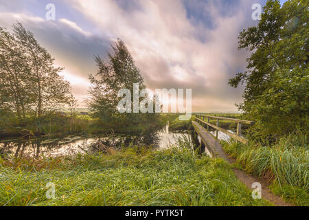 Footbridge  crossing river on a windy summer morning with fast moving clouds breaking open for the sun in september near Eelde, Drenthe, Netherlands Stock Photo