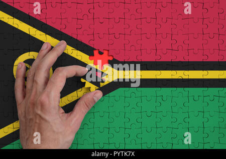 Vanuatu flag  is depicted on a puzzle, which the man's hand completes to fold. Stock Photo