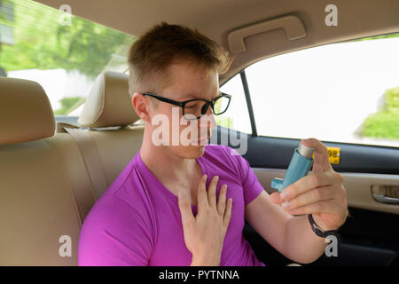 Man using asthma inhaler in back seat of car Stock Photo