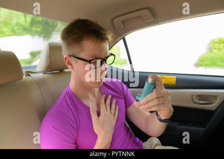 Man using asthma inhaler in back seat of car Stock Photo