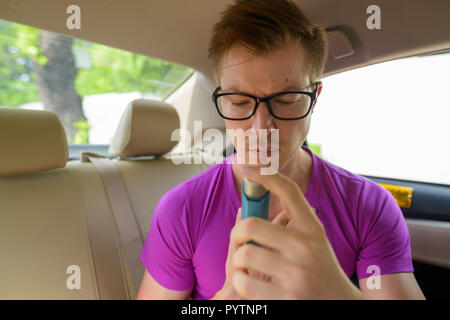 Face of man using asthma inhaler in back seat of car Stock Photo