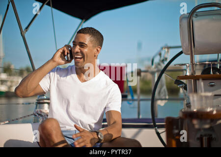 Smiling young man talking on his cell phone on a boat. Stock Photo
