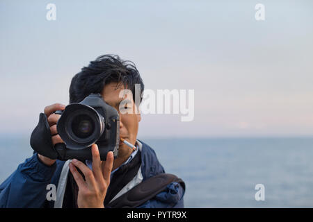 Young photographer with attitude takes photographs on the beach at sunset. Stock Photo