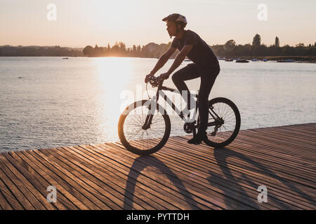 silhouette of man on bicycle in sunset city near lake, sport cycling active leisure Stock Photo