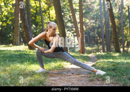 Sportish long-haired young woman wearing black shirt stretching in the sunny park, she listening music and enjoying of the good weather, healthy lifestyle and people concept Stock Photo