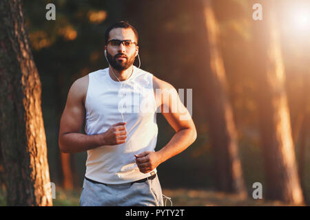 Multicultural handsome bearded man in sportswear listening his favorite music while jogging at the forest, healthy lifestyle and people concept Stock Photo