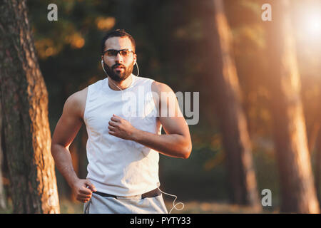 Multicultural handsome bearded man in sportswear listening his favorite music and having his morning running at the forest, healthy lifestyle and people concept Stock Photo