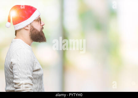 Young caucasian man wearing christmas hat and glasses over isolated background looking to side, relax profile pose with natural face with confident sm Stock Photo
