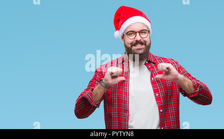Young caucasian man wearing christmas hat over isolated background looking confident with smile on face, pointing oneself with fingers proud and happy Stock Photo