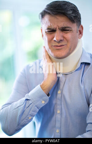 Mature Man Wearing Neck Brace Winces With Pain Stock Photo