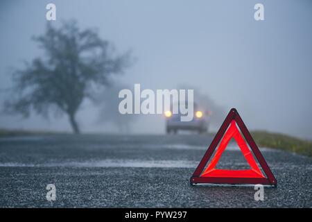 Traffic problem in thick fog. Car on the road behind warning triangle. Stock Photo