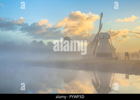 White wooden windmill at river in morning fog during sunrise, Drenthe, Netherlands Stock Photo