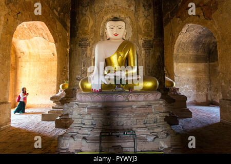 Tourist woman visiting a pagoda with a golden Buddha statue, Bagan, Myanmar Stock Photo