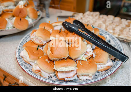 A pile of prepared turkey sandwiches stacked on a plate with tongs for serving. Stock Photo