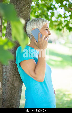Portrait of sporty senior woman using mobile phone in the park on sunny day Stock Photo
