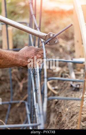 Worker Using Tools To Bend Steel Rebar At Construction Site. Stock Photo