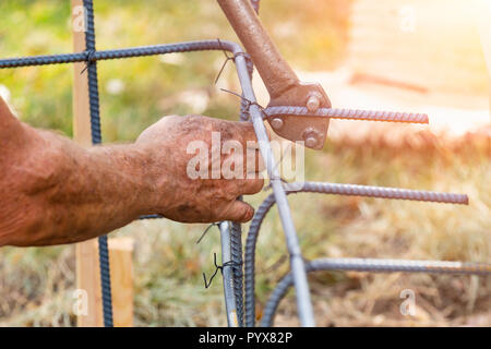 Worker Using Tools To Bend Steel Rebar At Construction Site. Stock Photo
