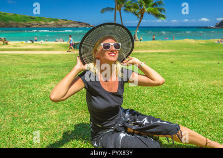Woman relaxing in Hanauma Bay Nature Preserve, Oahu, Hawaii, USA. Smiling female in black beachwear, floppy hat, sunglasses enjoying on hawaiian beach. Stock Photo