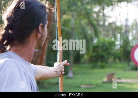 A male sport archer shooting an arrow with a bow at a red wooden target Stock Photo