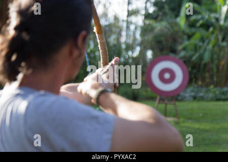 A male sport archer shooting an arrow with a bow at a red wooden target Stock Photo