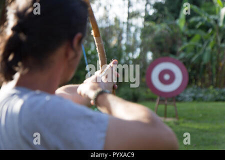 A male sport archer shooting an arrow with a bow at a red wooden target Stock Photo