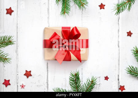 Gift box with red ribbon on wood background with pine branches. Top view. Stock Photo