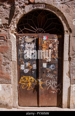 A weathered door covered in peeling paint, stickers, and graffiti, seen in Venice, Italy Stock Photo