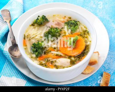 Italian vegetable soup with broccoli carrots noodles in chicken broth on blue table with slices of bread and glass juice. Food vegetarian organic stil Stock Photo
