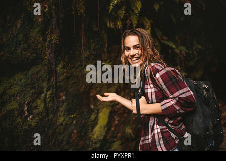 Portrait of beautiful young woman putting her hand under the water coming over from the rocks in forest. Cheerful woman enjoying a hike in rain forest Stock Photo