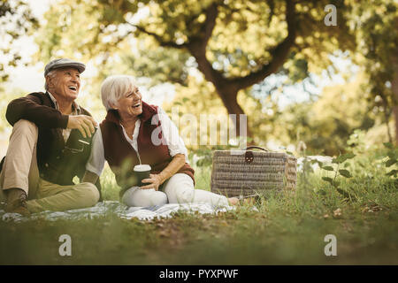 Smiling elder old couple sitting at the park with coffee and looking at a view. Senior couple having a great time together on a picnic. Stock Photo