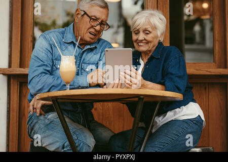 Happy retired couple sitting at coffee shop and using digital tablet. Old man and woman using tablet pc at cafe. Stock Photo