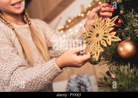 cropped image of preteen kid decorating christmas tree with golden snowflake at home Stock Photo