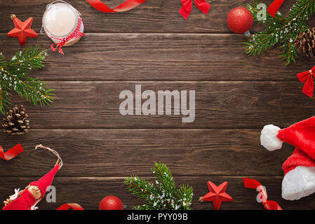 Christmas composition on wooden table. Fir branches, candle, Santa Claus hat, pinecones, doll, balls and stars beside. Copy space between. Stock Photo