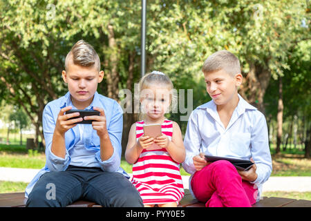 Group of busy kids looking at their phones texting sms and playing sitting outside Stock Photo