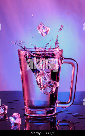Splashes of water. Falling ice cubes into a glass of water on a colored background Stock Photo
