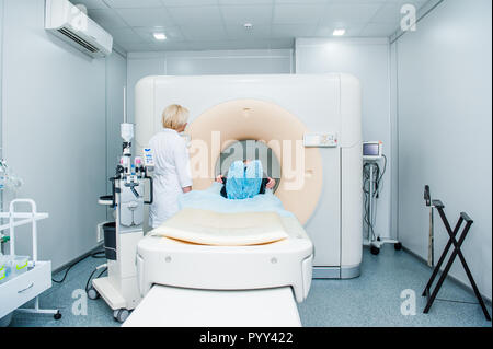 Female doctor adjusts computed tomography or computed axial tomography scan machine with lying patient in hospital room Stock Photo
