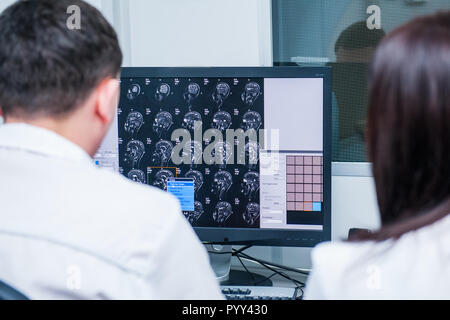 Doctors consider and discuss magnetic resonance image (MRI) of the brain. Back view, selective focus Stock Photo