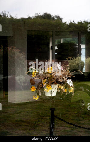 Vase of plastic flowers and wilted grass behind glass in an empty shop Stock Photo