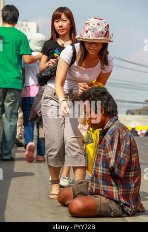Bangkok - 2010: A kind woman giving some money to a destitute on the busy streets Stock Photo