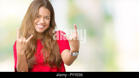 Young beautiful brunette woman wearing red t-shirt over isolated background shouting with crazy expression doing rock symbol with hands up. Music star Stock Photo