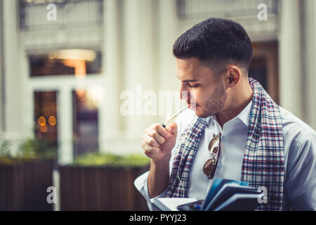 Young man wearing a white shirt is outside and he is lighting a cigarette Stock Photo